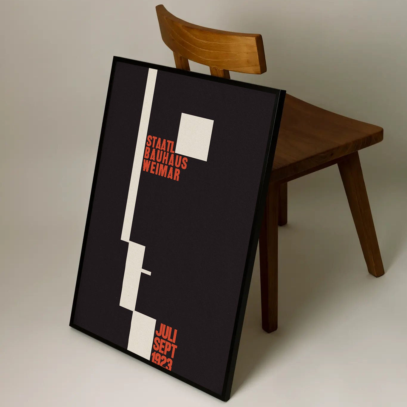 Framed poster leaning against a wooden chair on a plain background